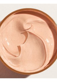 Crème cosmétique lisse et crémeuse de couleur pêche claire ou mousse, mélangée uniformément dans un récipient rond ouvert.
