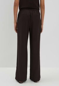 Zwarte broek met wijde pijpen, elastische tailleband, twee achterzakken, een soepele textuur en een losse pasvorm, gezien vanaf de achterkant.