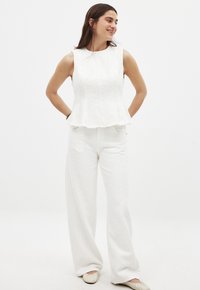 Top sin mangas texturizado blanco con un dobladillo peplum, combinado con pantalones anchos blancos. El conjunto presenta un sutil patrón tejido y un ajuste relajado.
