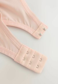 Blød lyserød bh-strop med tre-raders hægte- og øje-lukning på en lys baggrund, der viser syninger og stoftekstur.