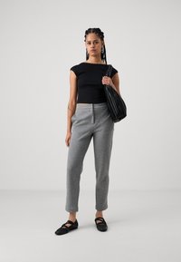 Svarte crop top, grå skreddersydde bukser og svarte flate sko. Utseendet har flettehår og en svart slapp bag med vertikale striper.