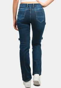 Jeans skinny-fit in denim blu scuro. Presentano cinque tasche, passanti per cintura e una texture scolorita. Indossati con sneakers bianche.