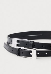 Svart lærbelte med en blank sølvspenne og flere hull for justering; glatt tekstur med pent søm og merkevaredetalj.