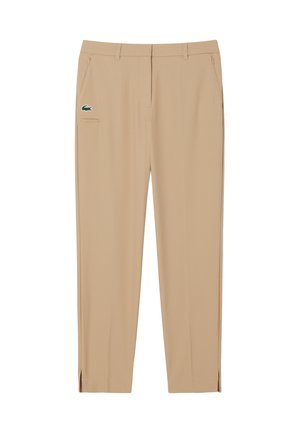 Pantalones beige con una textura suave, de corte slim, con bolsillos delanteros y un pequeño logo verde. Incluyen aberturas laterales en los dobladillos.