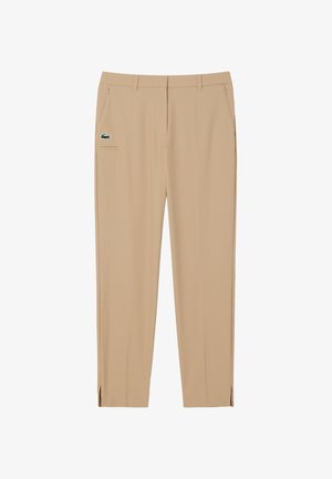 Pantaloni beige con una texture liscia, caratterizzati da una vestibilità slim, tasche frontali e un piccolo logo verde. Presentano spaccature laterali agli orli.