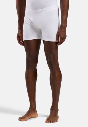Mannelijk model draagt witte geribbelde boxershorts, staat blootsvoets op een effen lichtgrijze achtergrond.
