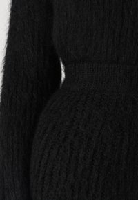 Black knit sweater with a fuzzy texture, featuring ribbed pattern and a fitted waist. Long sleeves taper at the wrists.