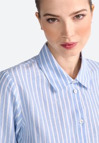 Lichtblauw en wit gestreept shirt met een kraag, knoopsluiting en korte mouwen, gemaakt van een textuur, ademende stof.