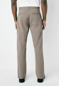 Beige trousers with a straight fit, two back pockets, and belt loops. Made of a smooth fabric, style features a slightly loose leg.
