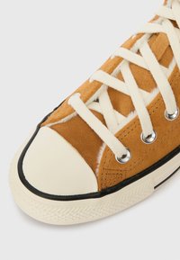 Καφέ σουέτ αθλητικά παπούτσια με λευκές κορδόνες, καπάκι από καουτσούκ στη μύτη, μαύρη περίμετρο και ασημένια μάτια κορδονιών; διαθέτουν υφή στο άνω τμήμα.