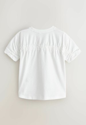Fehér pamut póló rövid ujjakkal, a hátán gyűrt részlettel. Sima textúra és laza szabás.