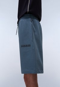 Light blue, cotton blend shorts with an elastic waistband, side pockets, and a black logo printed on the lower left side.