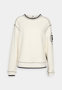 Kremowa bluza z teksturowaną tkaniną, czarnymi przeszyciami, ściągaczami na rękawach oraz naszywką z logo na lewym rękawie. Regularny krój.