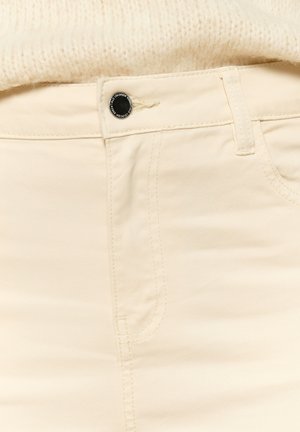 Beige katoenen jeans met een gladde textuur, voorzien van een zwarte knoopsluiting, gestikte zakken en zichtbare naden.