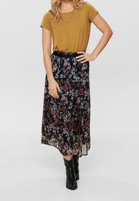 Jupe midi florale avec un fond bleu marine et des fleurs multicolores, associée à un haut  à manches courtes moutarde et une ceinture noire, portée avec des bottes noires.