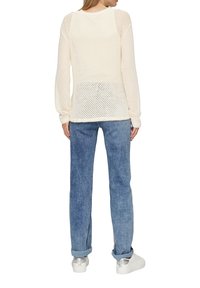 Licht crèmekleurig mesh langemouwtop met een losse pasvorm, gecombineerd met blauwe denim jeans en witte sneakers. Heeft een ronde halslijn en een textuurpatroon.