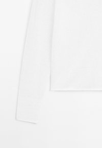 Pull en maille blanc à manches longues présenté à plat, montrant la manche gauche et la partie du torse sur fond blanc.