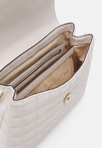 Světlá růžová prošívaná kabelka se zlatým kováním. Obsahuje několik přihrádek vystlaných béžovou látkou, včetně kapsy na zip a přihrádek na karty.