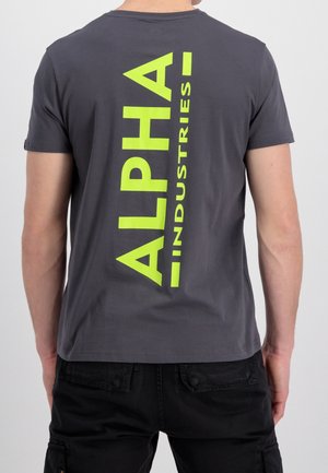 T-shirt grigio a maniche corte con un grande logo giallo "ALPHA INDUSTRIES" verticale sul retro. Realizzato in morbido cotone.