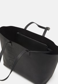 Borsa tote in pelle nera con doppi manici e nome del marchio traforato, aperta per mostrare la pochette nera con cerniera all'interno.