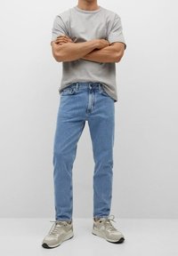 T-shirt in cotone grigio chiaro, vestibilità comoda. Jeans in denim blu, taglio dritto, lavaggio medio. Sneakers beige con dettagli grigi e lacci.