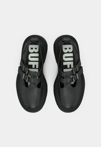 Fekete cipők sima bőrfelülettel, kivágott mintázattal, dupla pántos részlettel csatokkal és vastag "BUFF" logóval a fekete talpbetéteken.