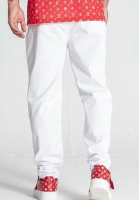 Pantaloni in denim bianco con una vestibilità rilassata, abbinati a sneaker rosse con motivo e loghi, con un focus sulla texture e sul contrasto dei colori.