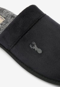 Sort slippers med en blød overflade, grå pelsforet indvendig og et diskret broderet hummer-logo. Flad sål med en rund form.