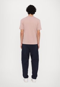 Lys rosa t-skjorte med rund hals og korte ermer, kombinert med mørk marineblå cargo-bukser med sidelommer, sett bakfra. Hvite joggesko.