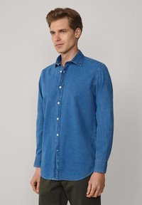 Blauwe spijkerblouse met een klassieke kraag, lange mouwen en knoopsluiting. Heeft een licht gebogen zoom en subtiele stikdetails.