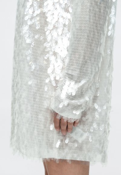 Διάφανο φόρεμα με μακριά μανίκια και επικάλυψη από λευκές παγιέτες, με υφή και μοτίβο στην επιφάνεια και χαλαρή εφαρμογή γύρω από τον καρπό.