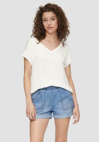 T-shirt bianco a V con maniche corte arrotolate, abbinato a pantaloni denim blu chiaro con vita elasticizzata e tasche frontali.