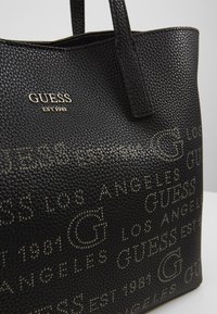 Sort tekstureret totebag lavet af syntetisk materiale. Har forhøjede logoer og brandnavnemønster, samt to robuste håndtag.