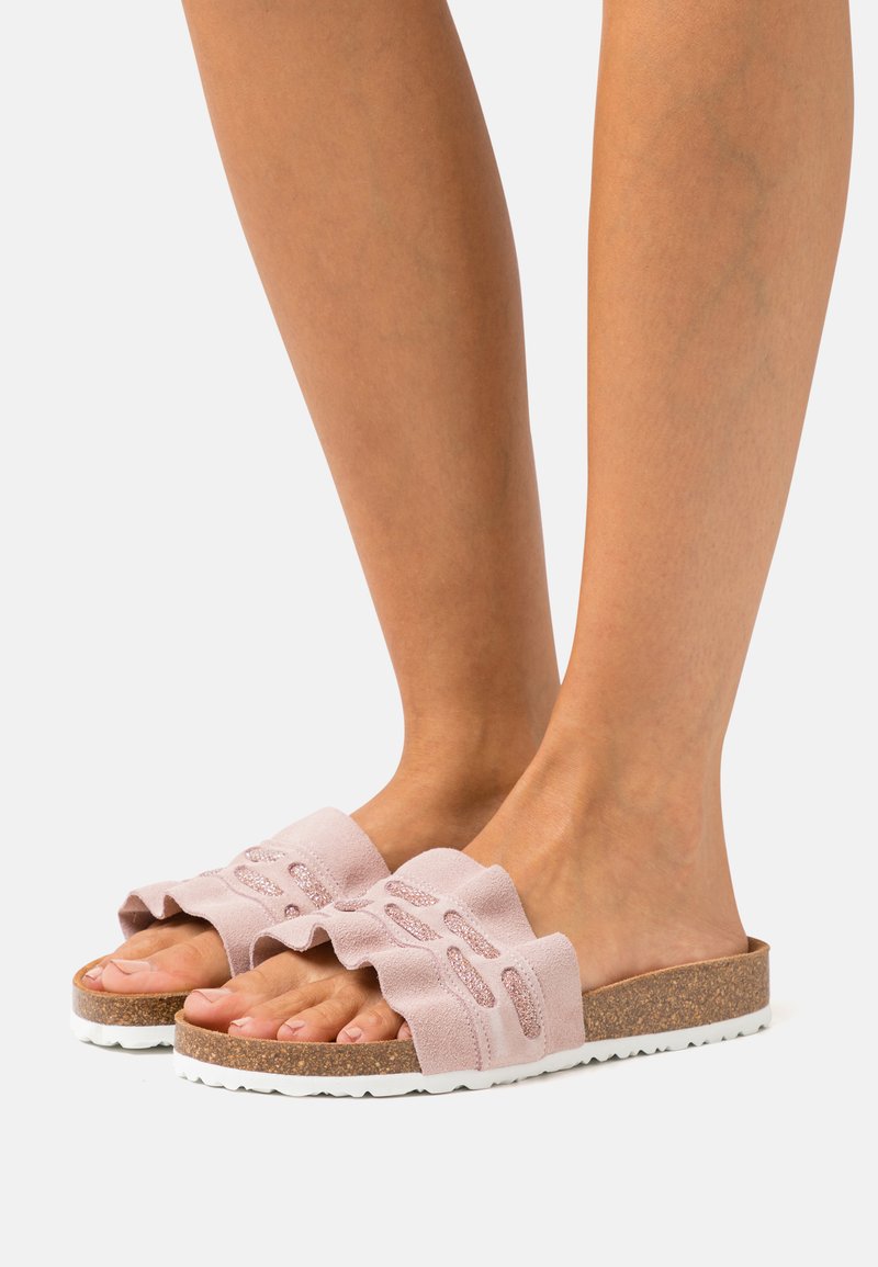 Rosa Wildlederschlupfschuhe mit einem gerafften Riemen, Korksohle und weißer Außensohle. Das offene Zehendesign zeigt Ausschnittmuster am Riemen.