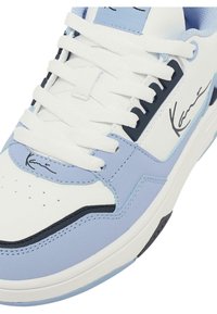 Fehér bőr felsőrészű sneaker, világoskék akcentusokkal és fekete részletekkel. Lapos fehér fűzőkkel rendelkezik, és a nyelv közelében található egy jellegzetes logó.