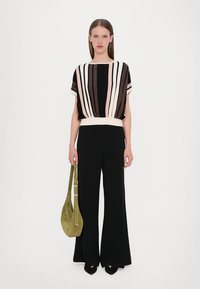 Striped knit top in black, cream, and pink, paired with black wide-leg trousers. Model holds an olive green suede bag.