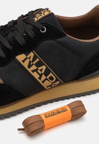 Sneaker nera con materiali in suede e sintetici, caratterizzata da un logo in cuoio beige, una tomaia texturizzata e un'etichetta arancione sui lacci marroni coordinati.