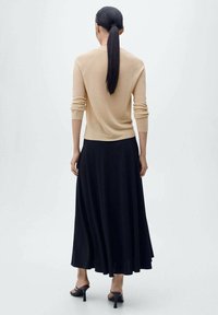 Beige, aansluitende trui met lange mouwen, gecombineerd met een vloeiende zwarte maxi rok. Gladde textuur, minimalistisch ontwerp en enkelschoenen met bandjes.