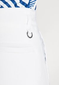 White denim skirt featuring a flat waistband with a silver hardware accent and a side pocket detail. Smooth texture with clean stitching.