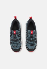 Scarpe sportive con tomaia in rete traspirante di colore blu scuro, con accenti neri e dettagli rossi. Stringhe elastiche e colletto imbottito. Suola bianca.