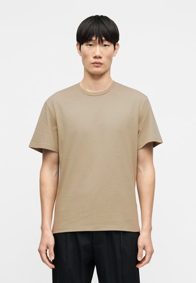 T-shirt en coton beige avec un col rond, des manches courtes et une coupe décontractée. Présente une texture lisse et un design minimaliste.