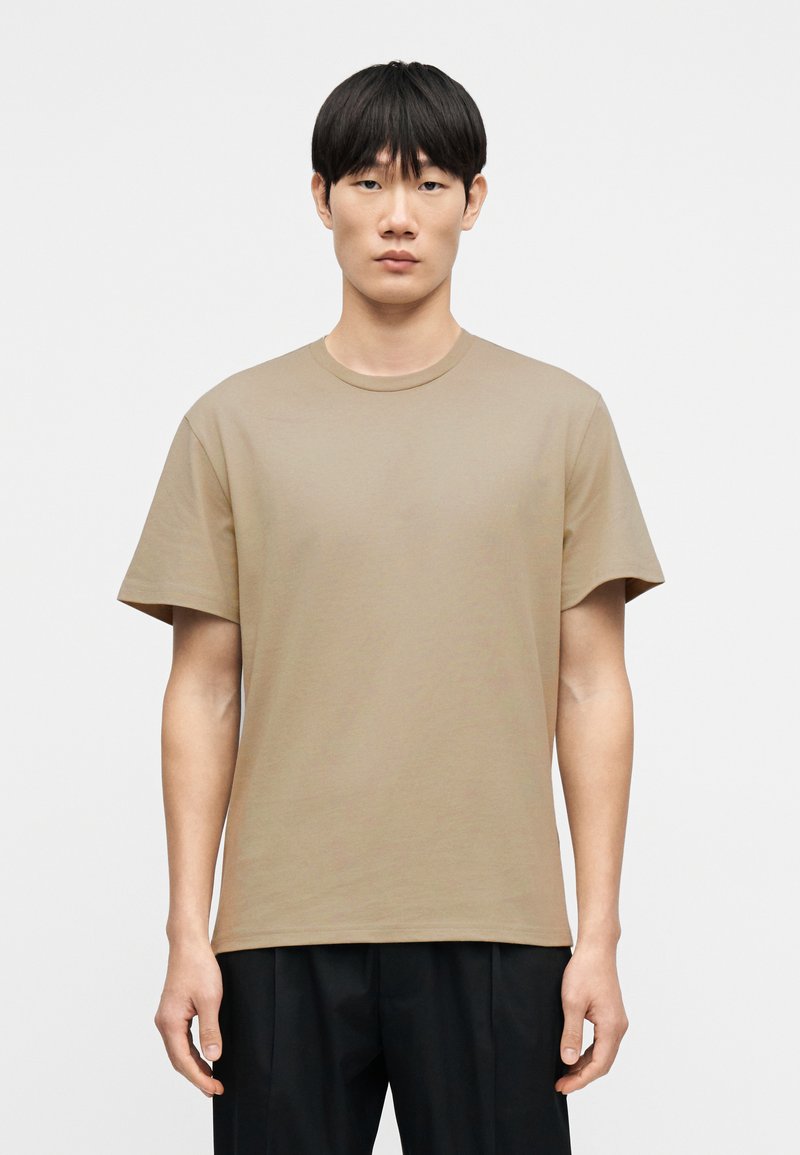 Μπεζ βαμβακερό μπλουζάκι με στρογγυλή λαιμόκοψη, κοντά μανίκια και άνετη εφαρμογή. Διαθέτει απαλή υφή και μινιμαλιστικό σχέδιο.