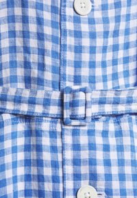 Blå och vit rutigt tyg med matchande tygspänne och vita knappar på ett plagg.