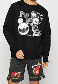 Felpa nera con grafica bianca "Nets" e motivi di pallacanestro. Abbinata a pantaloni corti neri con il logo "Heat" colorato e dettagli in rilievo.