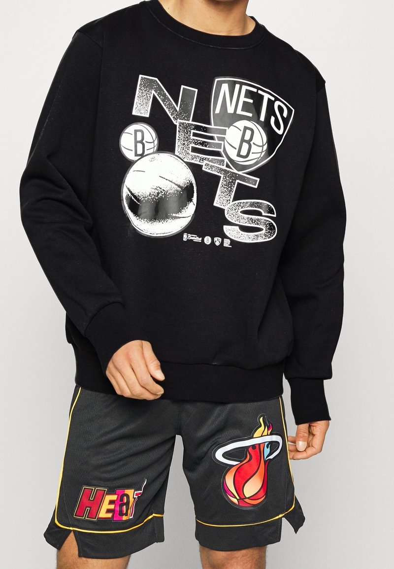 Felpa nera con grafica bianca "Nets" e motivi di pallacanestro. Abbinata a pantaloni corti neri con il logo "Heat" colorato e dettagli in rilievo.