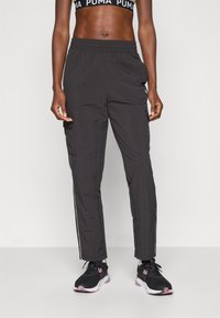 Melni sporta bikses ar elastīgu jostu, šauru piegriezumu un kontrastējošām sānu svītrām. Valkā ar melnu sporta krūšturi un treniņu apaviem.