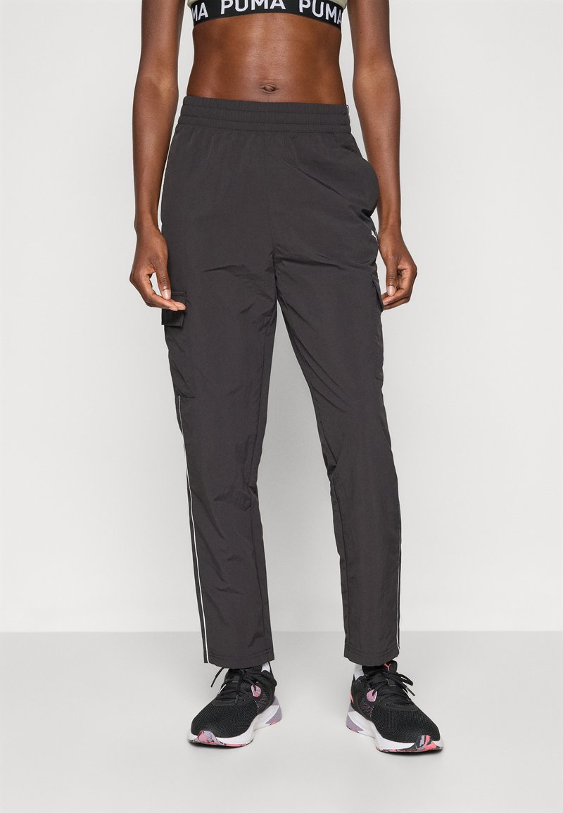 Melni sporta bikses ar elastīgu jostu, šauru piegriezumu un kontrastējošām sānu svītrām. Valkā ar melnu sporta krūšturi un treniņu apaviem.