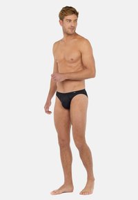Zwarte bikini briefs voor mannen met een gladde textuur, elastische tailleband en minimale bedekking. De stof lijkt lichtgewicht en aansluitend.