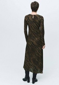 Vestido de manga larga en color verde oliva oscuro con rayas de tigre negras, que cuenta con un detalle de corte en la espalda y una silueta fluida, combinado con botas altas hasta la rodilla.