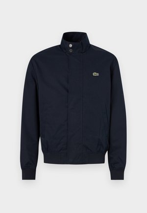 Veste pour homme bleu marine avec col montant, boutons-pression sur le devant, deux poches latérales, poignets côtelés et petit logo crocodile vert sur la poitrine.